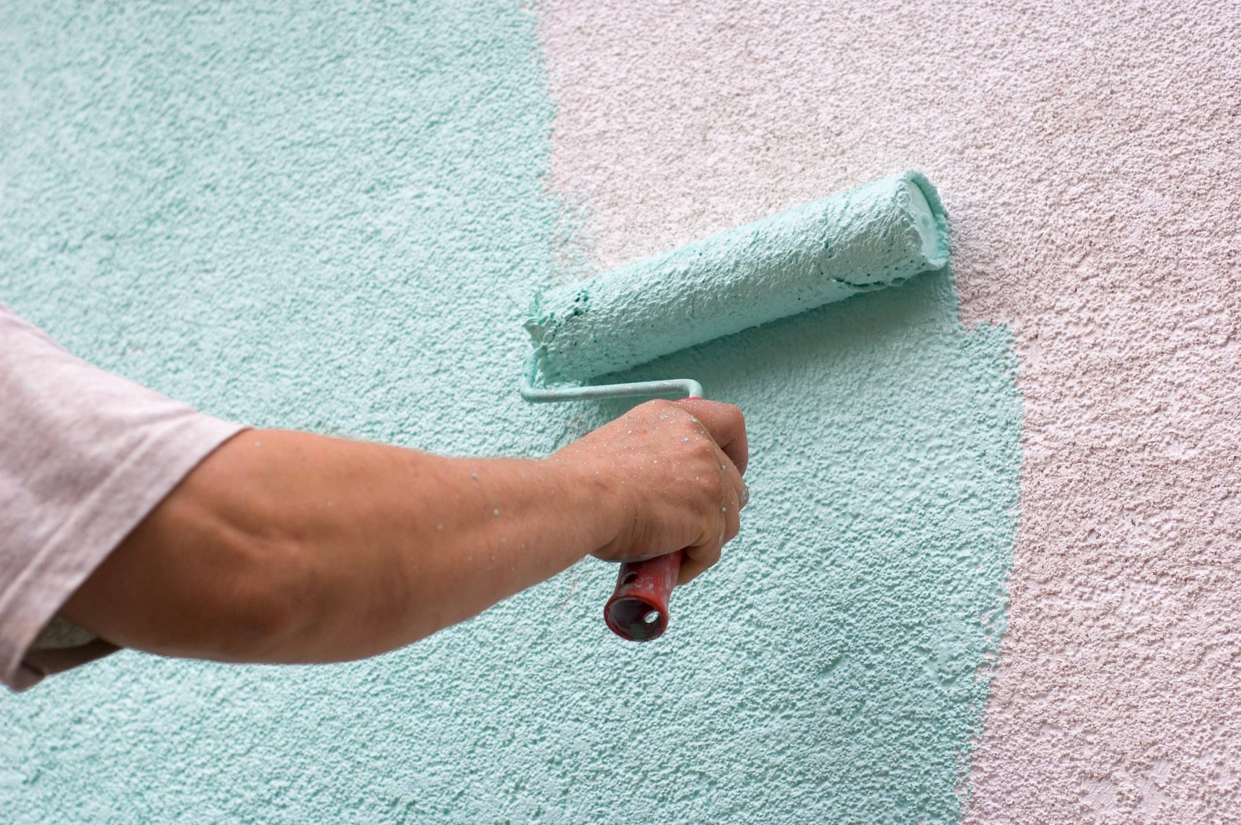 Roller applying fresh paint over textured stucco