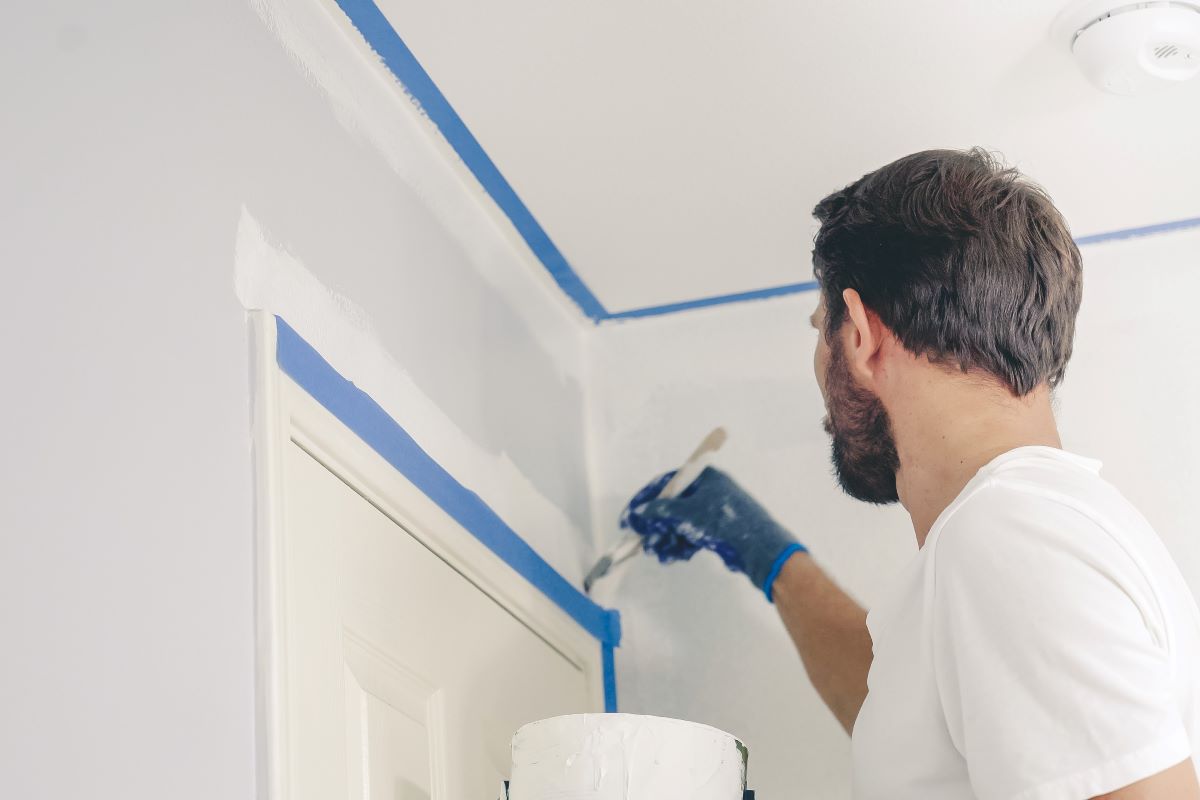 Painter cutting in along blue painters tape before rolling