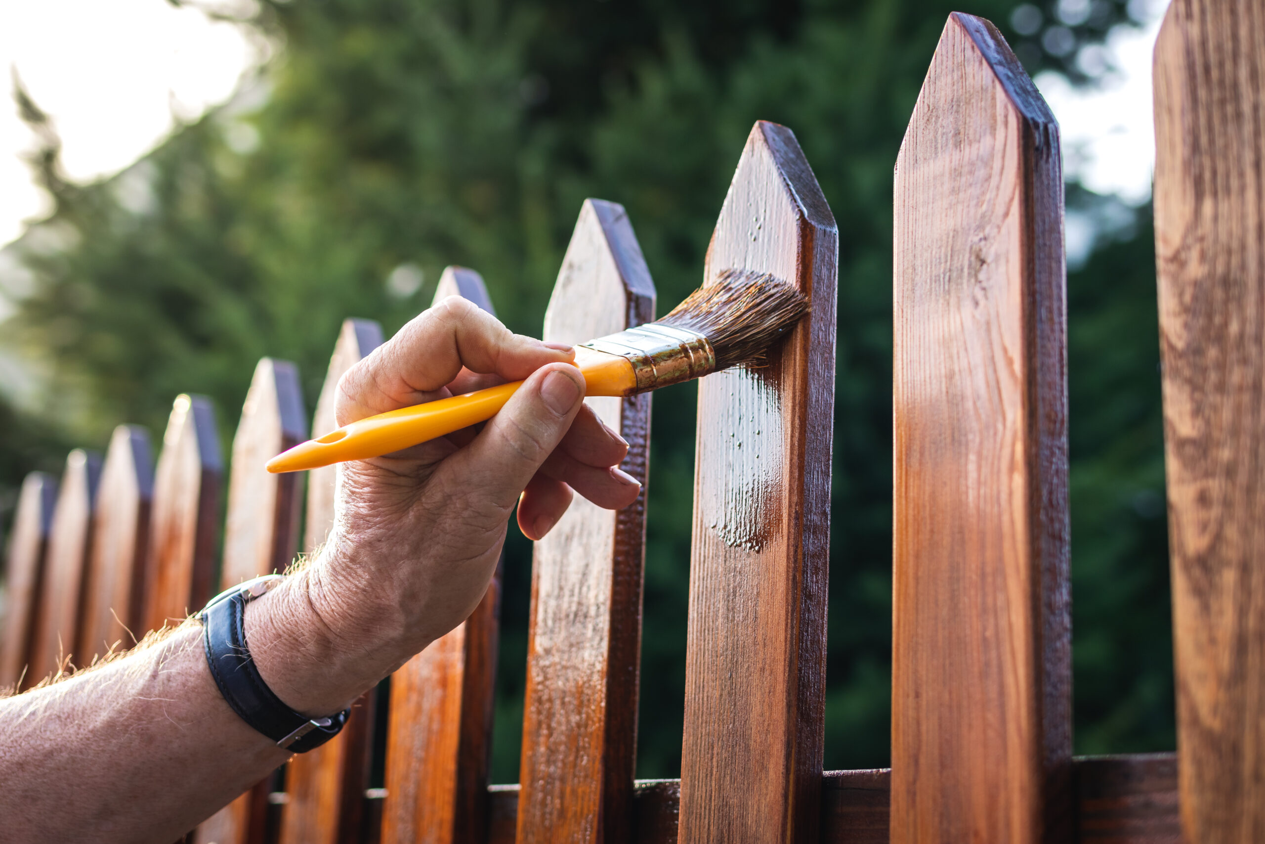 Brush applying stain to the pickets of a wood fence