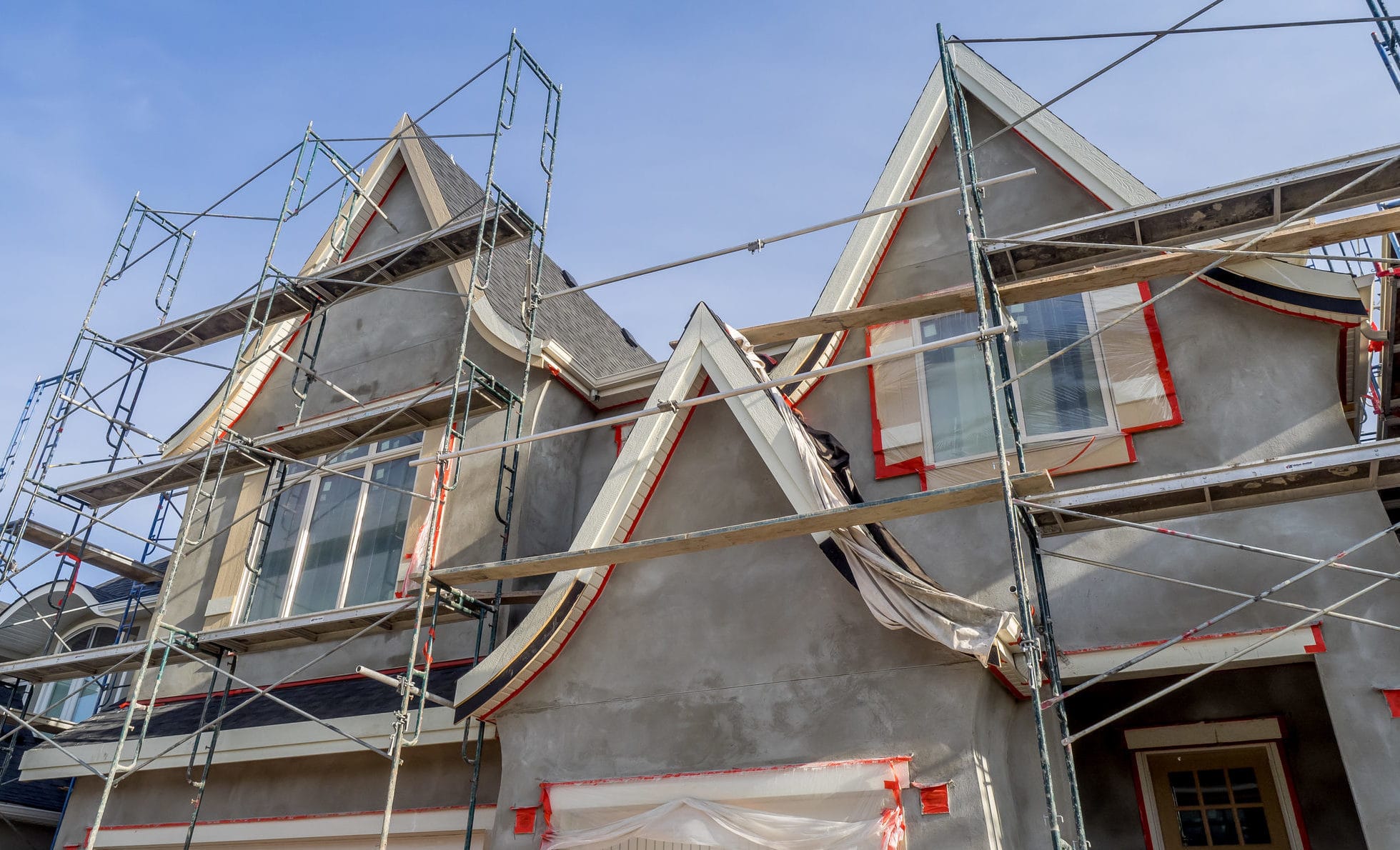 Painter spraying a textured stucco wall with windows masked